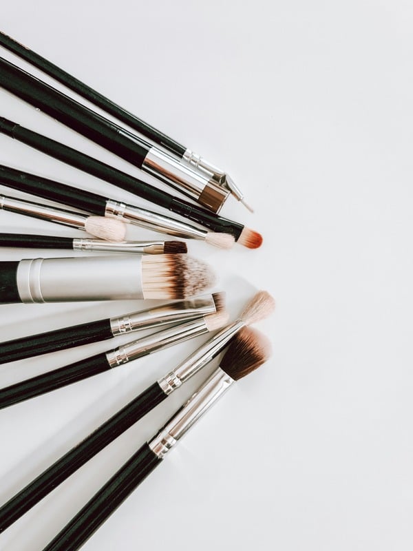 A fan of black-handled makeup brushes on a pale background